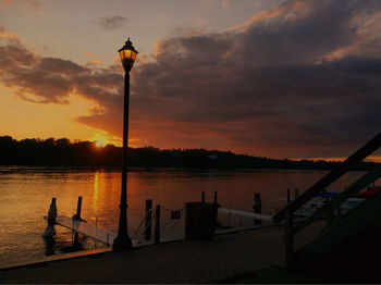 Silhouette street light by lake against sky during sunset