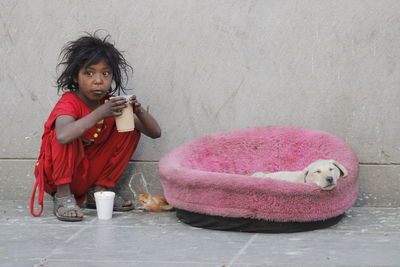 Girl holding drink looking away while sitting with puppy on sidewalk