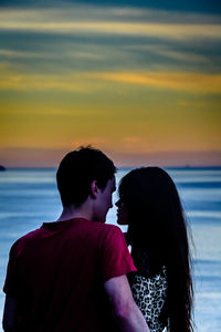 Rear view of couple on shore against sky during sunset