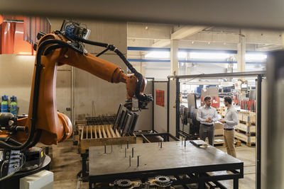 Business people having discussion while standing by automated robotic arm at factory