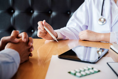 Midsection of doctor holding thermometer by patient on table at hospital