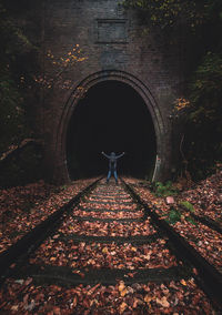 Mid distance view of man standing on railroad track by tunnel in forest during autumn
