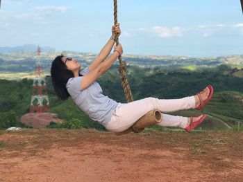 Full length of woman swinging on hill against sky