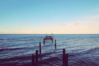 Wooden posts in sea against sky