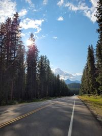 Empty road by trees against sky