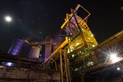 Low angle view of illuminated factory against sky at night