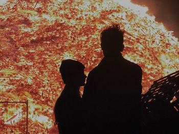 Silhouette of man and woman standing against fire at night