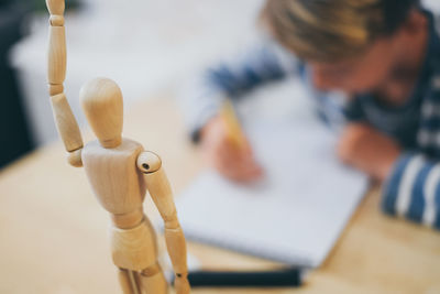 Close-up of wooden figurine with boy making sketch in background