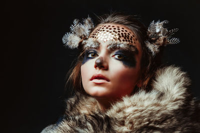 Close-up of young woman with make-up and fur against black background