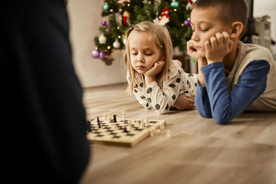 Boy and girl lying on floor looking at chess board at home