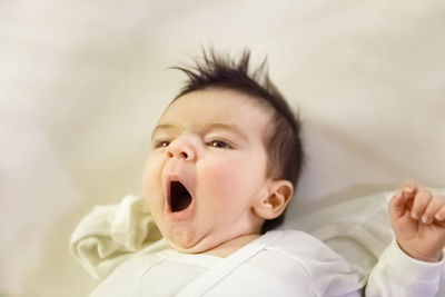 High angle view of cute baby boy yawning while lying on bed at home