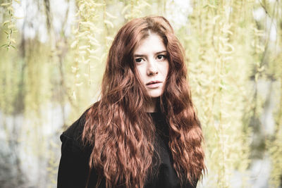 Beautiful redhead young woman under the willow tree lookin at the camera. outdoor portrait.