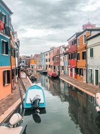Boats moored in canal by buildings against sky