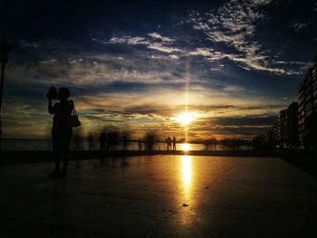Silhouette people standing in city against sky during sunset