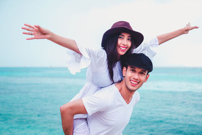 Portrait of smiling husband piggy backing wife while standing at beach