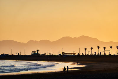 Silhouette people on beach against clear sky during sunset