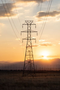 Low angle view of electricity pylon on field against sky during sunset