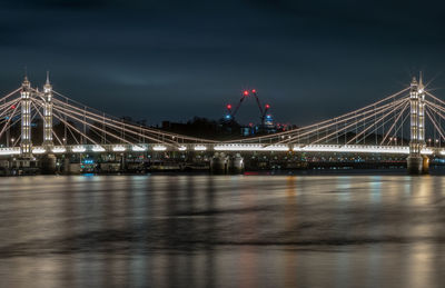 Illuminated bridge over river against sky at night