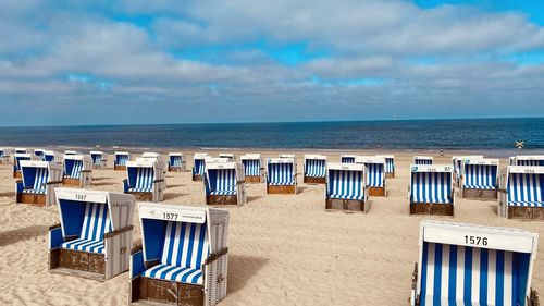 Hooded chairs on beach against sky