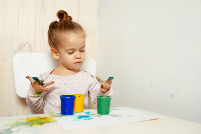 Cute girl with messy hands with water color paints while sitting on table