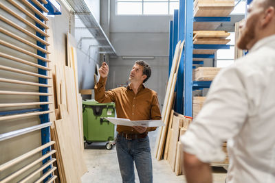 Two carpenters talking while examining planks in production hall