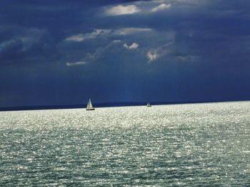 Boat sailing in sea against cloudy sky