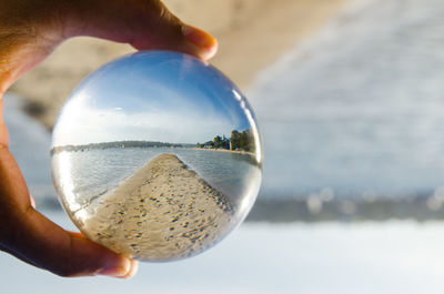 Close-up of human hand holding crystal ball against sea