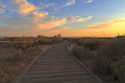 Boardwalk on beach against sky during sunset