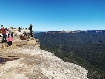 People on rocks against mountain range against clear sky