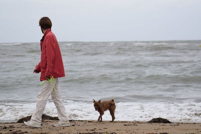 Mid adult man with dog walking at beach against sky