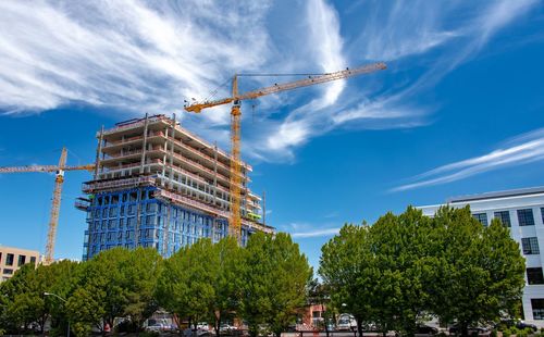 Low angle view of crane by building against blue sky