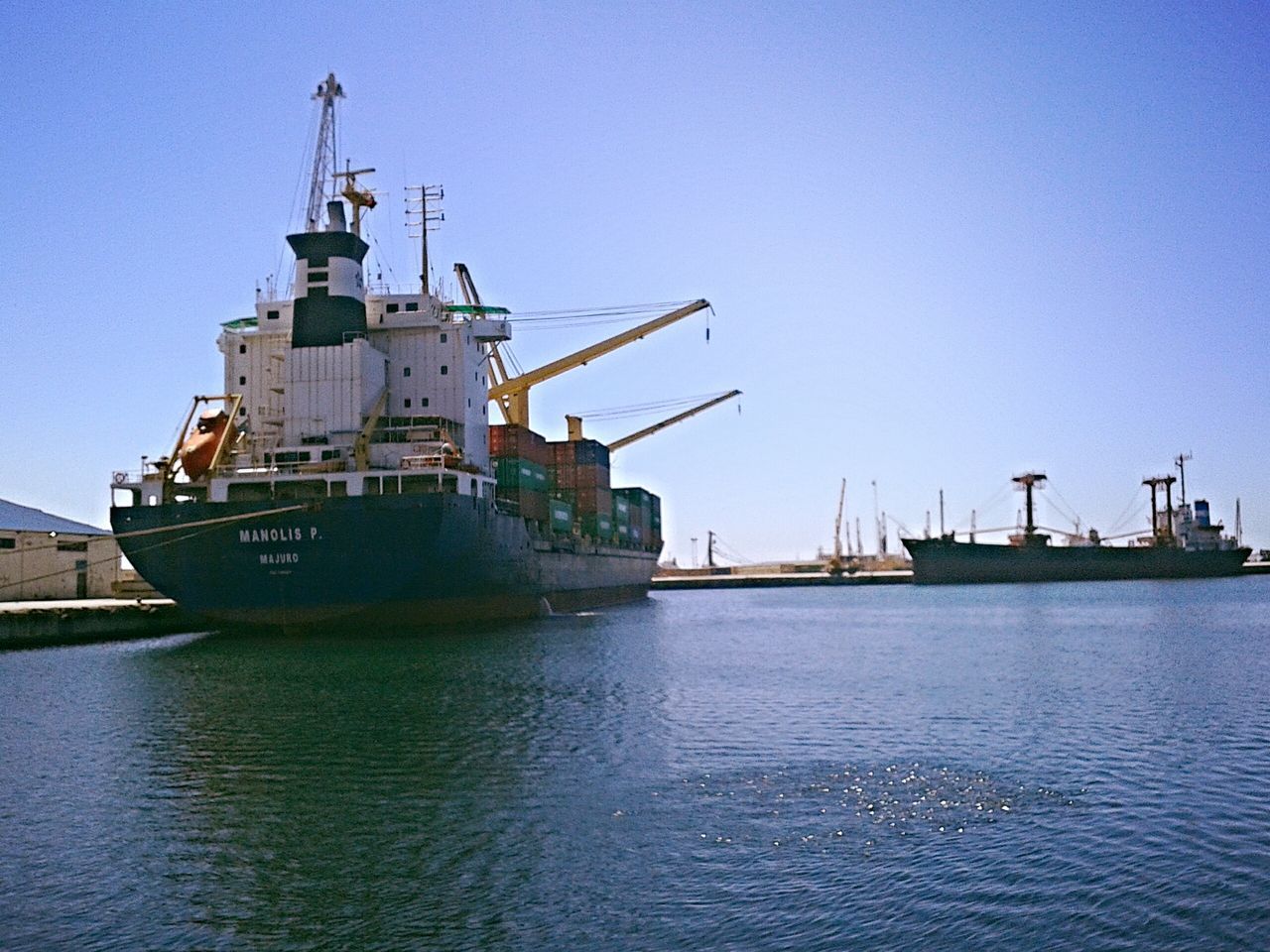 water, clear sky, crane - construction machinery, waterfront, nautical vessel, commercial dock, harbor, transportation, copy space, mode of transport, crane, built structure, sea, freight transportation, industry, building exterior, blue, renewable energy, ship, architecture