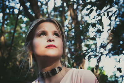 Young woman looking away against trees