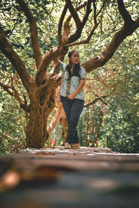 Full length of woman standing by tree trunk