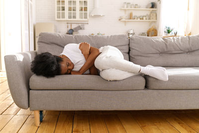 Depressed unhappy black woman lying on couch at home, crying, suffering from divorce or break up.