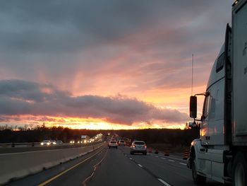 Cars on road against dramatic sky during sunset