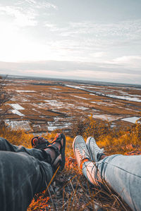 Low section of people relaxing on land against sky