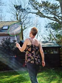 Rear view of woman standing against trees in yard