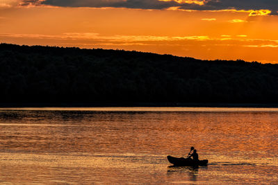 Silhouette people in boat on lake against orange sky