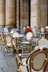 Empty chairs and tables at sidewalk cafe by building