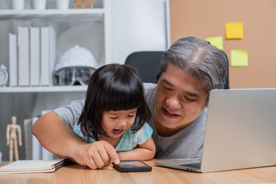 Girl and grandfather looking in smart phone at table