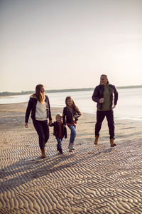 Family in a leather jacket run along the beach with their dog in autumn