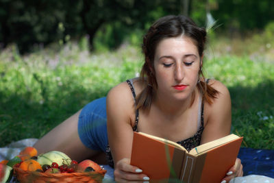 Young woman reading book while lying down in park