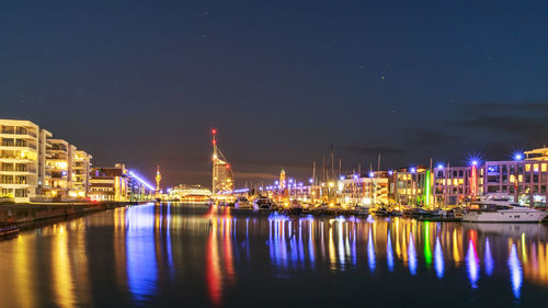 Illuminated buildings by river against sky at night