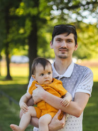 Caucasian handsome happy young dad holding in his arms his little daughter in yellow bodysuit