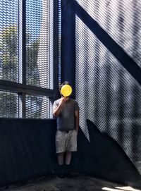 Front view of man holding yellow balloon against windows and wall.