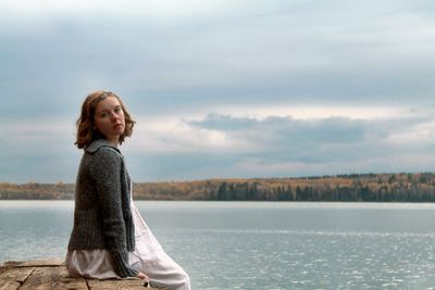 Portrait of young woman sitting on pier over sea against sky