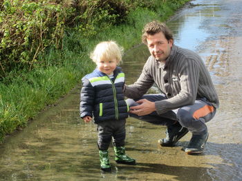 Father and son exploring the puddles together in the countryside.