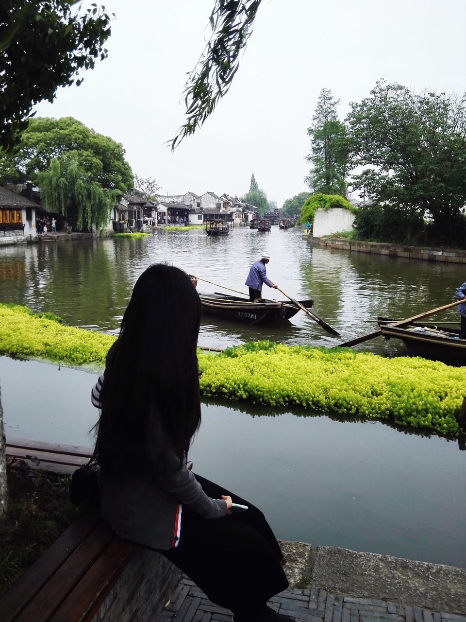 water, lifestyles, leisure activity, rear view, lake, tree, men, sitting, river, person, nautical vessel, clear sky, casual clothing, full length, nature, transportation, standing, reflection