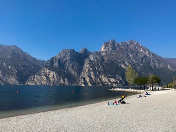 People on mountain by sea against clear blue sky